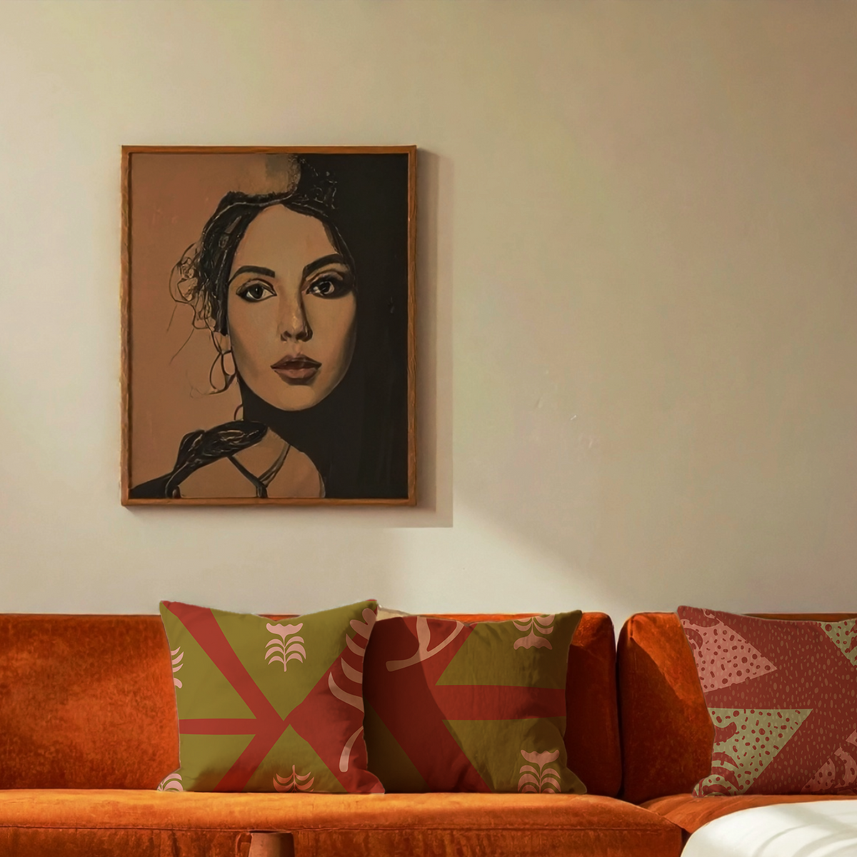 A framed portrait painting of a woman hangs on a beige wall above an orange sofa with patterned green and red throw pillows.