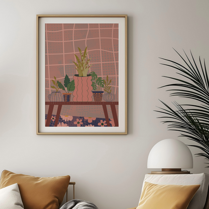 A framed art print featuring a stylized illustration of potted plants on a table against a pink grid background, displayed on a light gray wall above a sofa with pillows and a lamp.
