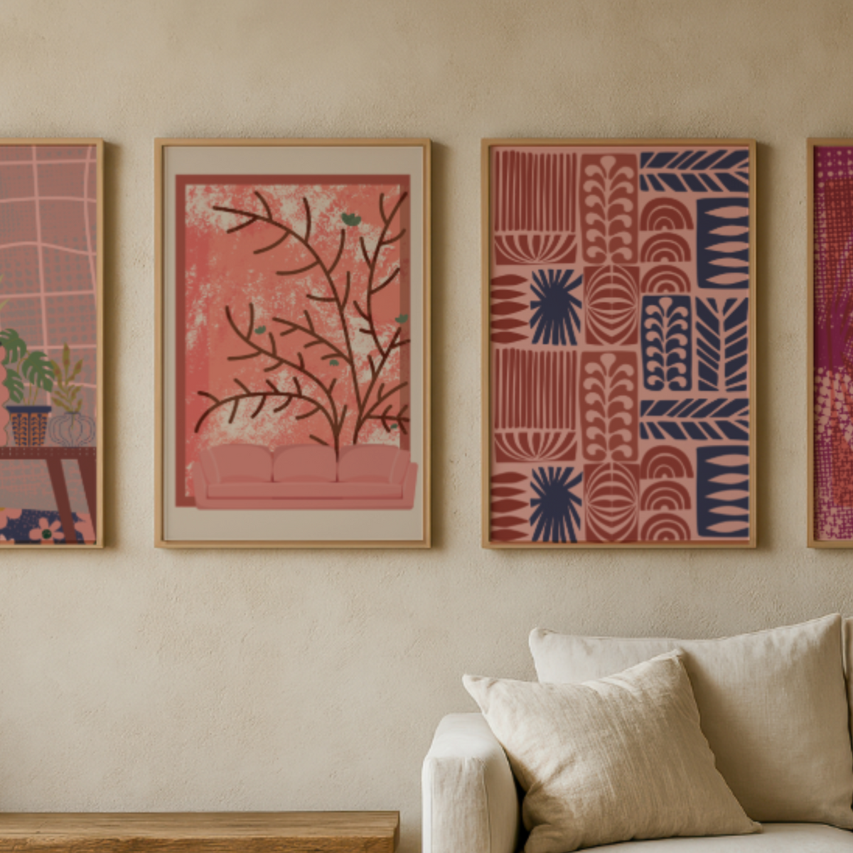 Three framed abstract art prints in pink, red, and navy tones hang on a beige wall above a light-colored sofa with pillows.
