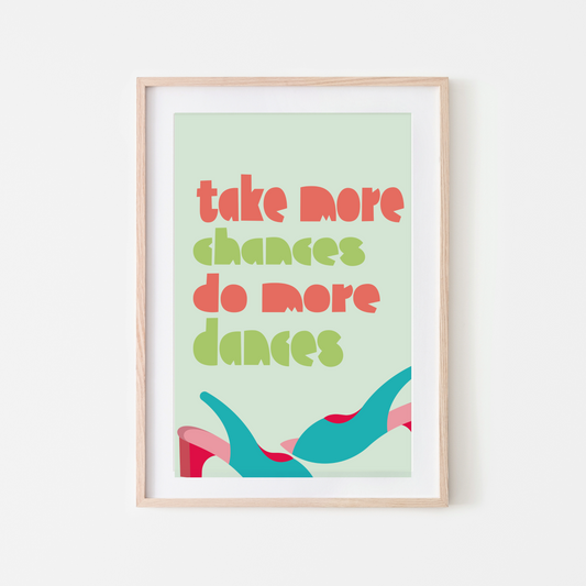 Framed wall art print with the motivational quote "Take More Chances, Do More Dances" in bold, colourful typography on a light green background, featuring abstract shapes.
